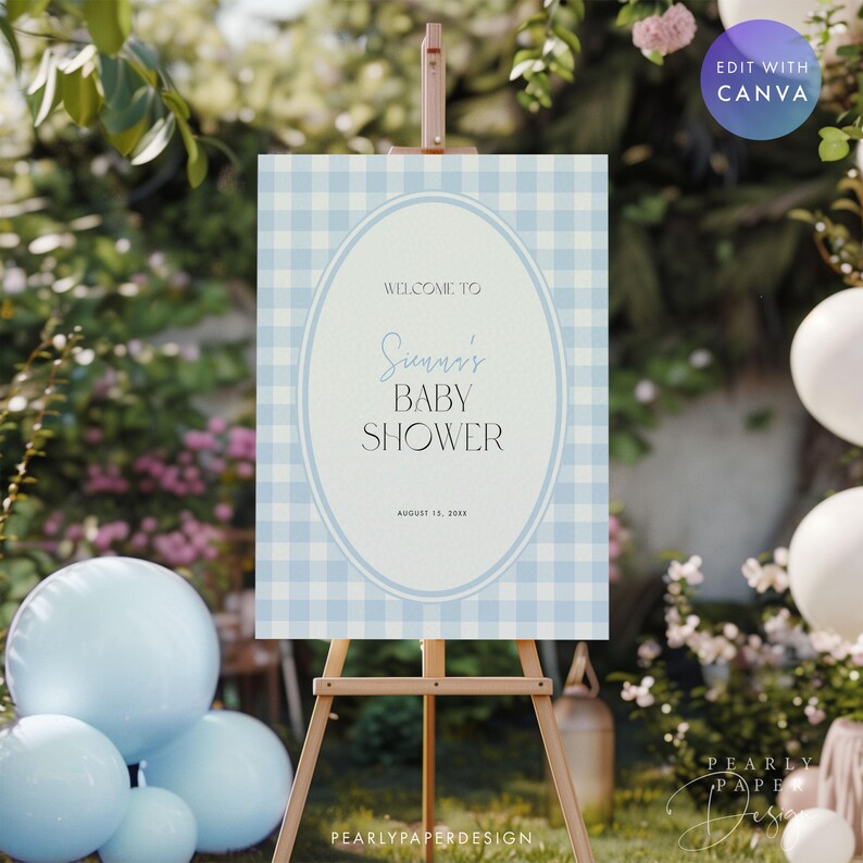 May include: A baby shower sign on a wooden easel. The sign has a light blue and white gingham pattern background with an oval frame. Text reads "Welcome to [Name]'s Baby Shower" and the date. Balloons and greenery are in the background.