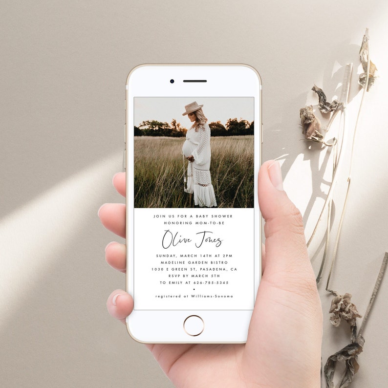 May include: A white smartphone screen displays a baby shower invitation for Olive Jones. The invitation includes the date, time, location, and RSVP information. A photo of a pregnant woman in a white dress is in the background.
