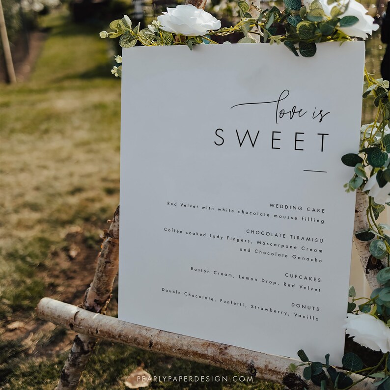 Puede incluir: Un cartel blanco con texto negro que dice "Love is Sweet" y enumera pastel de bodas, tiramis&uacute; de chocolate, cupcakes y donas. El cartel est&aacute; apoyado en un caballete de madera.
