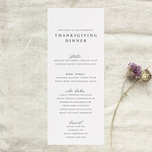 May include: A Thanksgiving dinner menu with a handwritten font. The menu includes appetizers, main course, side dishes, and dessert. The menu items include roasted butternut squash salad, seasoned roasted turkey with white wine and rosemary gravy, garlic whipped potatoes, sweet potato casserole with homemade marshmallow, fresh herb stuffing, green beans with bacon, honey butter cornbread, pecan slab pie, pumpkin pie, apple cheddar pie, coffee and tea.