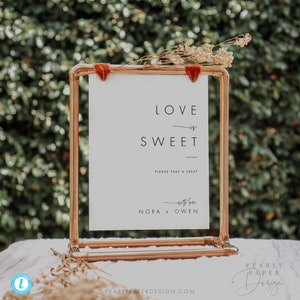 May include: A white sign with the text "LOVE is SWEET" in black, displayed in a copper-coloured frame. The sign includes the text "PLEASE TAKE A TREAT" and "with love NORA + OWEN". Dried flowers and red velvet accents adorn the top.