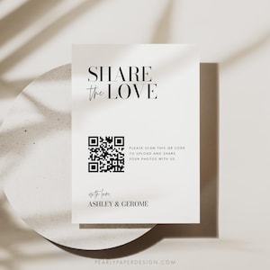 May include: A white card with black text that reads "SHARE the LOVE". A black and white QR code is below the text with the instructions "PLEASE SCAN THIS QR CODE TO UPLOAD AND SHARE YOUR PHOTOS WITH US". The text "with love, ASHLEY & GEROME" is below the QR code. The text "PEARLYPAPERDESIGN.COM" is at the bottom of the card.