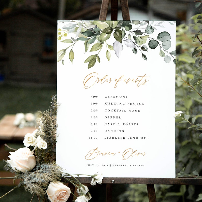 May include: A white wedding sign with green foliage and gold lettering. The sign lists the order of events for a wedding, including the ceremony, wedding photos, cocktail hour, dinner, cake and toasts, dancing, and a sparkler send off. The sign also includes the couple's names, "Diabea Oliver", and the date and location of the wedding, "July 25, 2020 | Beaulieu Gardens".
