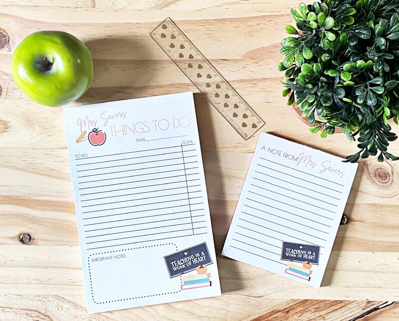 May include: Two white notepad sets with lined paper. The top notepad has the text "Mrs. Severs Things To Do" with a red apple and pencil illustration. The bottom notepad has the text "A Note From Mrs. Severs". Both notepads have a black and white illustration of a chalkboard with the text "Teaching is a work of heart".