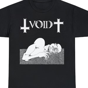 May include: Black t-shirt featuring a white graphic. The graphic includes the word "VOID" above a stylized illustration of a figure lying down. The word "VOID" is flanked by inverted crosses.
