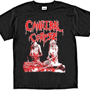 Peut inclure: T-shirt noir avec un motif rouge du groupe Cannibal Corpse. Le motif représente deux personnages dans une scène sanglante avec le nom du groupe en grandes lettres rouges.