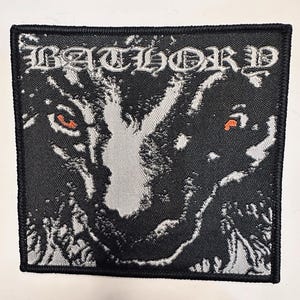 May include: Square black patch with the word "BATHORD" in white gothic lettering. The patch features a detailed illustration of a wolf's face with red eyes and a textured design.