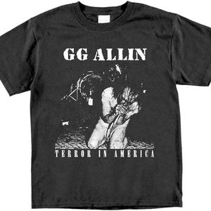 May include: Black t-shirt with a white graphic of GG Allin, a musician, performing on stage. The text "Terror in America" is printed below the image.