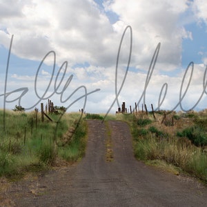 May include: A dirt road leading up a hill with a wooden fence on either side. The sky is blue with white clouds.
