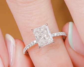 May include: A close-up of a hand wearing a silver ring with a large, rectangular, clear diamond. The ring is set on a thin band with small diamonds.
