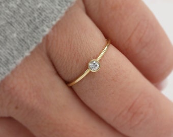 May include: A simple gold band ring with a single, small, round, clear gemstone.