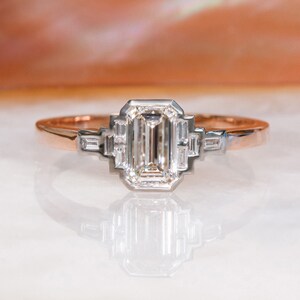 Puede incluir: Un anillo de compromiso de oro rosa con un gran diamante de talla esmeralda engastado en un engaste de oro blanco. El anillo presenta un dise&ntilde;o delicado con diamantes m&aacute;s peque&ntilde;os en la banda.