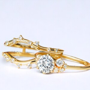 May include: A pair of gold rings with a delicate, vine-like design. The larger ring features a round, clear diamond in the center, surrounded by smaller diamonds.