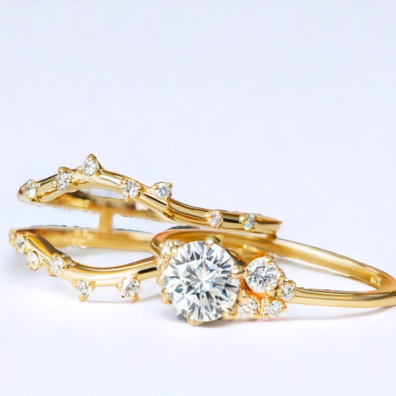 May include: A pair of gold rings with a delicate, vine-like design. The larger ring features a round, clear diamond in the center, surrounded by smaller diamonds.