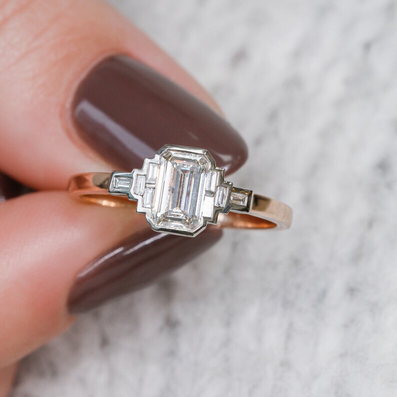 Puede incluir: Un anillo de compromiso de oro rosa con un gran diamante de talla esmeralda y diamantes baguette m&aacute;s peque&ntilde;os en la banda.