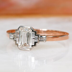 Puede incluir: Un anillo de compromiso de oro rosa con un gran diamante de talla esmeralda y diamantes baguette m&aacute;s peque&ntilde;os en la banda.