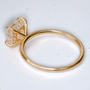 Puede incluir: Un anillo de oro con un gran diamante de forma cuadrada engastado en garras. El diamante est&aacute; rodeado de diamantes m&aacute;s peque&ntilde;os.