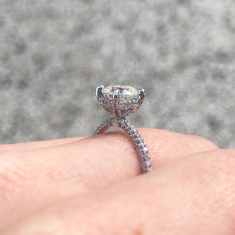 K&ouml;nnte beinhalten: Ein silberner Verlobungsring mit einem gro&szlig;en ovalen Diamanten als Mittelst&uuml;ck und einer doppelten Reihe kleinerer Diamanten um das Band.