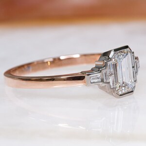 Puede incluir: Un anillo de compromiso de oro rosa con un diamante cuadrado de talla esmeralda y diamantes baguette m&aacute;s peque&ntilde;os en la banda.