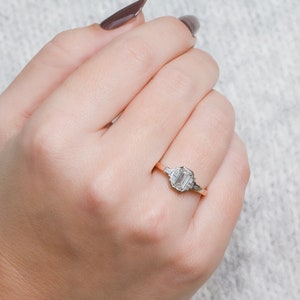 Puede incluir: Un delicado anillo de oro con un diamante rectangular de talla esmeralda y dos diamantes m&aacute;s peque&ntilde;os en la banda.