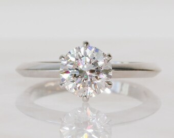 May include: A silver engagement ring with a large, round, clear diamond.