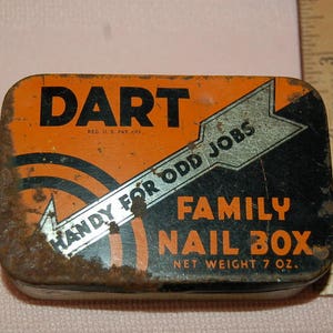 May include: A vintage metal tin box for nails, labeled "DART" in black letters on an orange background. The tin has a black and white arrow with the text "HANDY FOR ODD JOBS" and "FAMILY NAIL BOX" in white letters on a black background. The tin is rusty and has a net weight of 7 ounces.