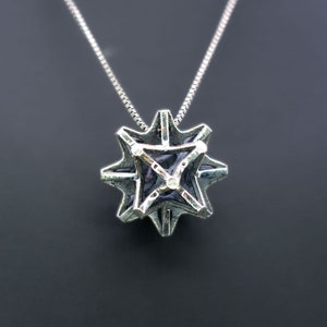 May include: A silver necklace with a geometric pendant. The pendant is a star shape with a black centre and silver lines. The pendant is approximately 2.5 cm in diameter.