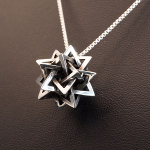 May include: A silver chain necklace with a geometric star-shaped pendant. The pendant is made of multiple interlocking triangles.