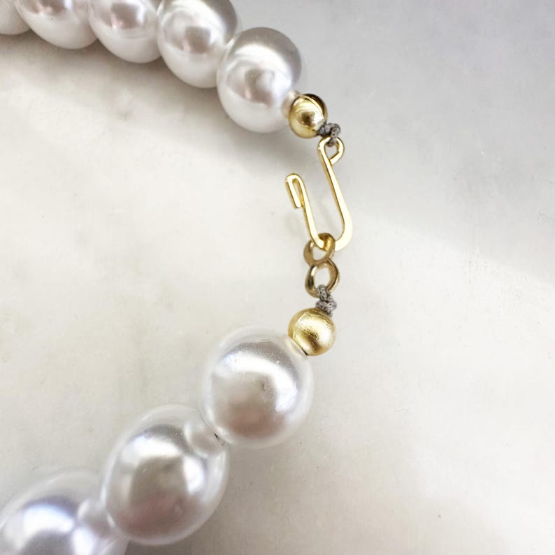 Puede incluir: Un collar de perlas blancas con un cierre dorado. Las perlas son grandes y redondas.