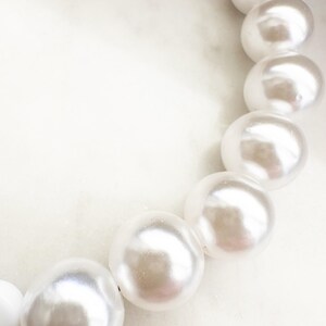 Puede incluir: Primer plano de un collar de perlas blancas con perlas grandes y redondas. Las perlas est&aacute;n enhebradas en un hilo transparente y est&aacute;n dispuestas en un dise&ntilde;o simple y elegante.