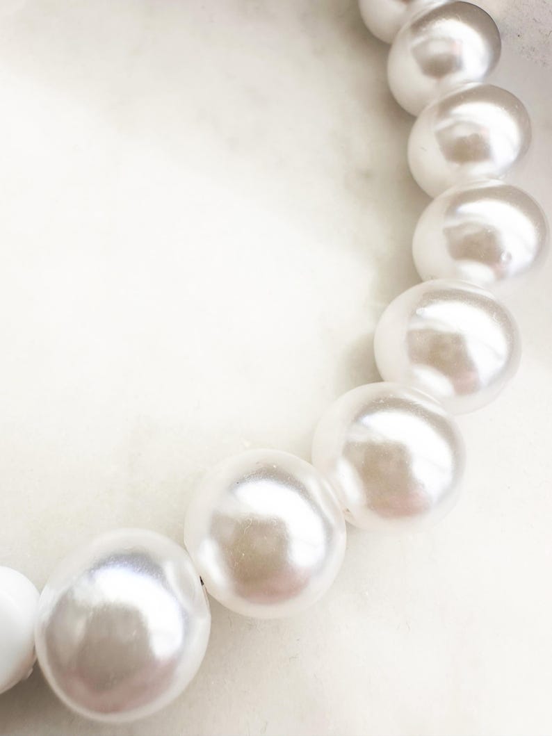 Puede incluir: Primer plano de un collar de perlas blancas con perlas grandes y redondas. Las perlas est&aacute;n enhebradas en un hilo transparente y est&aacute;n dispuestas en un dise&ntilde;o simple y elegante.