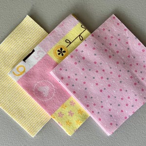 May include: A collection of four square fabric napkins. One is yellow with a textured pattern, another is pink with white and gray polka dots. The other two have floral and geometric designs in yellow, pink, and white.