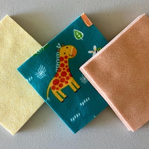 May include: Three square fabric pieces in a row. One is pale yellow, one is teal with a giraffe print, and the last is peach with a herringbone pattern. The fabrics are likely for crafting or quilting.