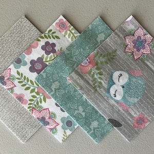 May include: Four square paper napkins arranged in a diagonal overlapping row. The first is grey with a white pattern, the second features pink and purple flowers, the third is teal with a floral print, and the fourth shows owls and flowers.