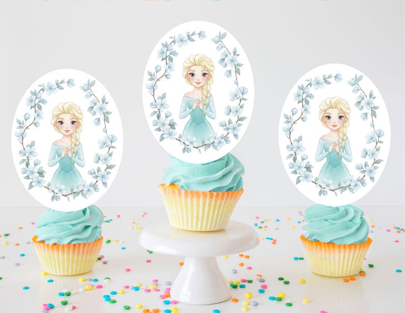 Op de afbeelding: Drie cupcakes met blauwe glazuur en gele vormpjes zijn bekroond met ovale afbeeldingen van een blonde vrouw in een blauwe jurk, omringd door blauwe bloemen. E&eacute;n cupcake staat op een witte taartstandaard, met hagelslag verspreid.