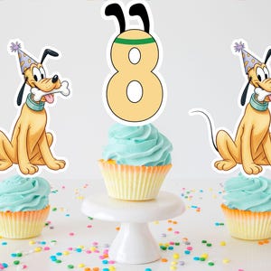 Puede incluir: Una exhibición de pastel de cumpleaños con tres cupcakes con glaseado azul y envoltorios amarillos. Se incluyen recortes del perro Pluto y un adorno para pastel con el número 8. Hay chispas de colores esparcidas.