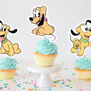 Peut inclure: Trois cupcakes avec un glaçage bleu clair et des caissettes jaunes. Chaque cupcake est surmonté d'une découpe de personnage de chien de dessin animé. Un chien est assis, un autre court et un autre tire la langue. Les cupcakes sont sur une surface blanche.