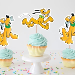 May include: Cupcakes with light blue frosting and Pluto-themed toppers. The yellow cartoon dog is featured in three different poses, with a bone in his mouth in two of the poses. The cupcakes are on a white cake stand and table.