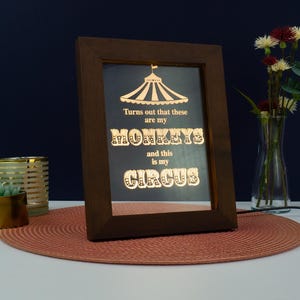 May include: A framed light-up sign with a gold-colored design. The sign reads "Turns out that these are my monkeys and this is my circus".