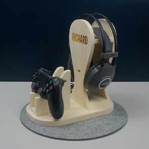 May include: A wooden stand with the name "RICHARD" engraved on it. The stand is designed to hold a pair of black headphones and a black video game controller.