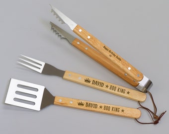 May include: A set of three barbecue tools with wooden handles and stainless steel heads. The set includes tongs, a spatula, and a fork. The handles are engraved with "Happy Birthday Daddy" and "DAVID BBQ KING".
