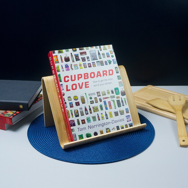 K&ouml;nnte beinhalten: Ein Kochbuch mit dem Titel "Cupboard Love: How to get the most out of your kitchen." von Tom Norrington-Davies. Der Umschlag zeigt eine bunte Collage von Lebensmitteln.