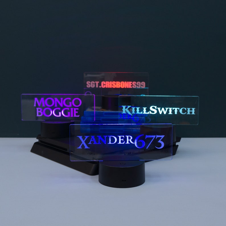 May include: Four illuminated acrylic signs with different names on them. The signs are on black bases and are lit up in different colours. The names on the signs are "MONGO BOGGIE", "SGT.CRISBONESS99", "KILLSWITCH", and "XANDER673".