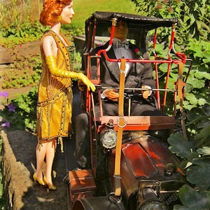 Puede incluir: Un coche rojo y negro vintage con capota de lona negra. Una mujer con un vestido amarillo y un hombre con un traje negro están sentados en el coche.