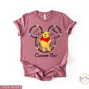 May include: Heather mauve t-shirt featuring a Winnie the Pooh design. The design includes a Mickey Mouse silhouette with the text "2026 Aunt" and "Custom Text". Winnie the Pooh is wearing a red shirt. The shirt has a crew neck.