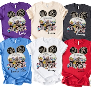 May include: A collection of colorful t-shirts featuring a Disney's Hollywood Studios design. Each shirt has a unique color and personalized text, including names like "Emily," "Daddy," and "Grandma." The design includes Mickey Mouse ears and cartoon characters.