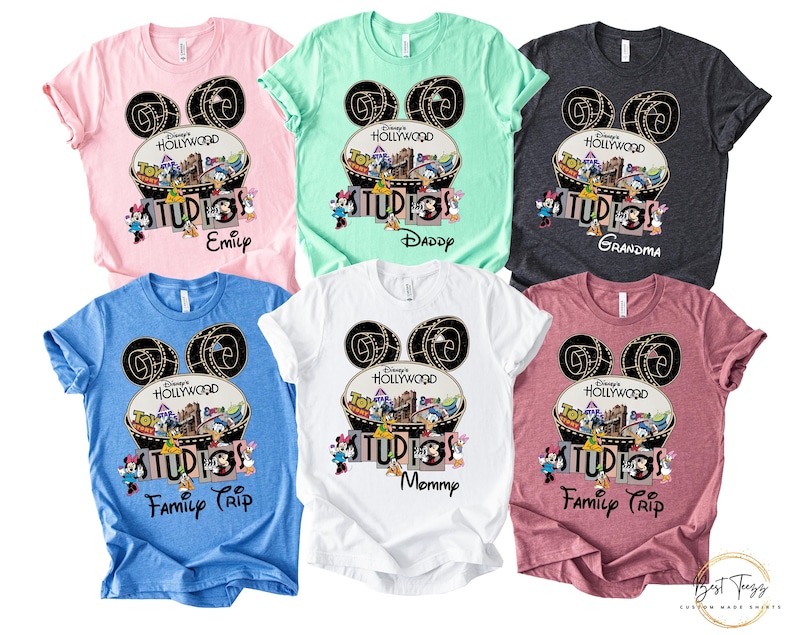 May include: Assorted-color t-shirts featuring a Disney's Hollywood Studios design. Each shirt has a Mickey Mouse ear design with the text "Hollywood Studios" and a family member's name or phrase like "Family Trip".