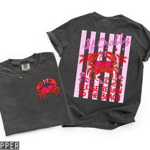 K&ouml;nnte beinhalten: Zwei dunkelgraue T-Shirts mit Strandmotiv. Ein Shirt zeigt einen kleinen, gestickten roten Krebs mit Sonnenbrille. Das andere Shirt hat eine gro&szlig;e Grafik eines Krebses mit Sonnenbrille und dem Text "If Crabby, Please Return to the Beach."