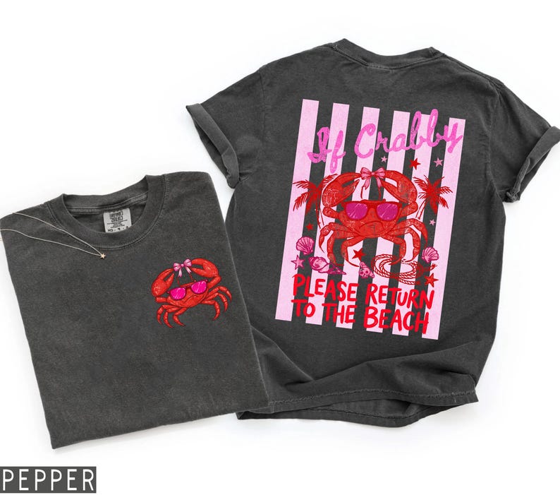 K&ouml;nnte beinhalten: Zwei dunkelgraue T-Shirts mit Strandmotiv. Ein Shirt zeigt einen kleinen, gestickten roten Krebs mit Sonnenbrille. Das andere Shirt hat eine gro&szlig;e Grafik eines Krebses mit Sonnenbrille und dem Text "If Crabby, Please Return to the Beach."