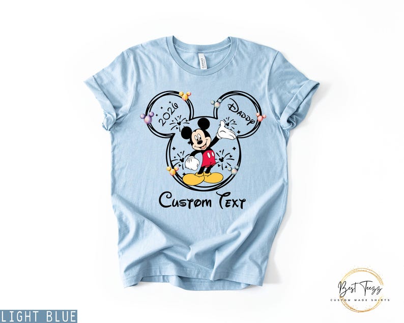 May include: Light blue t-shirt featuring a Mickey Mouse graphic with the text "2020 Daddy" inside a Mickey Mouse head outline. The shirt also includes the words "Custom Text" below the graphic.
